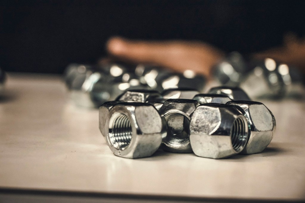 A pile of chrome lug nuts on a table with a blurred hand in the background