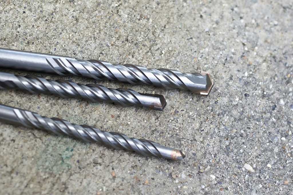 Three masonry drill bits lying on a rough concrete surface