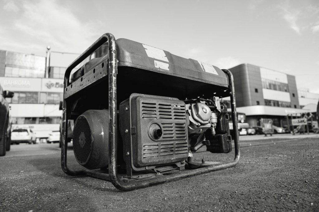 Black-and-white photo of an open-frame portable gas generator sitting on pavement outdoors